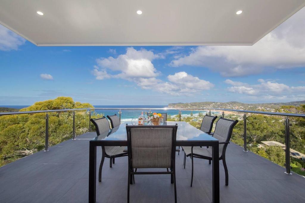 a dining table on a balcony with a view of the ocean at Avoca Infinity - Expansive Haven with Ocean Panorama in Terrigal