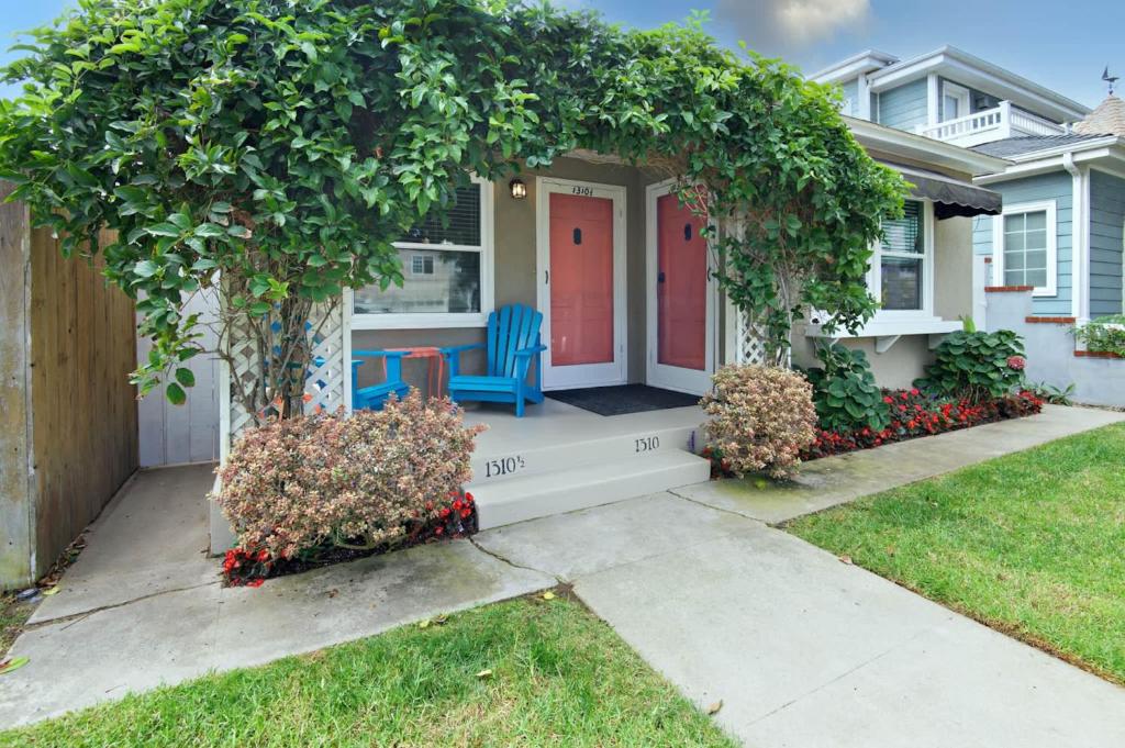 a house with a red door and blue chairs on a porch at Charming Beach Bungalow in Seal Beach