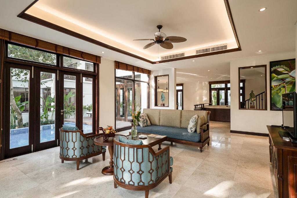 A sunlit villa living room with a sofa, lounge chairs and glass doors to the pool area.