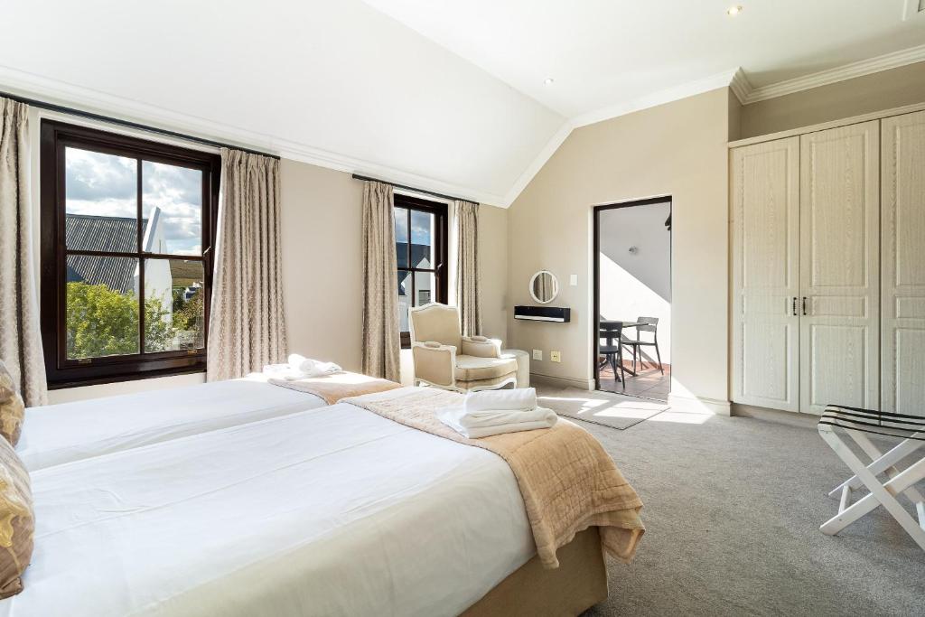 a white bedroom with a large bed and a chair at Winelands Golf Lodges 15 in Stellenbosch