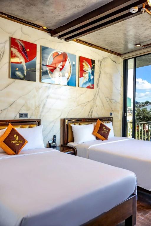 two beds in a room with paintings on the wall at khách sạn phúc hải in Da Lat
