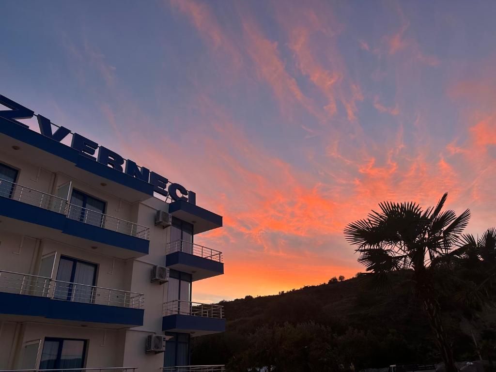 a hotel with a palm tree in front of a sunset at Hotel Zverneci in Vlorë