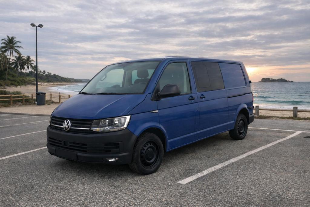 a blue van parked in a parking lot next to the ocean at La Vallena Camper in Madrid
