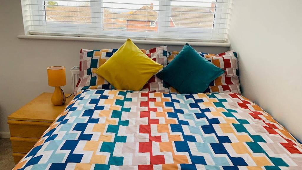 a bed with colorful pillows and a window at A cosy & peaceful homestay in Sutton