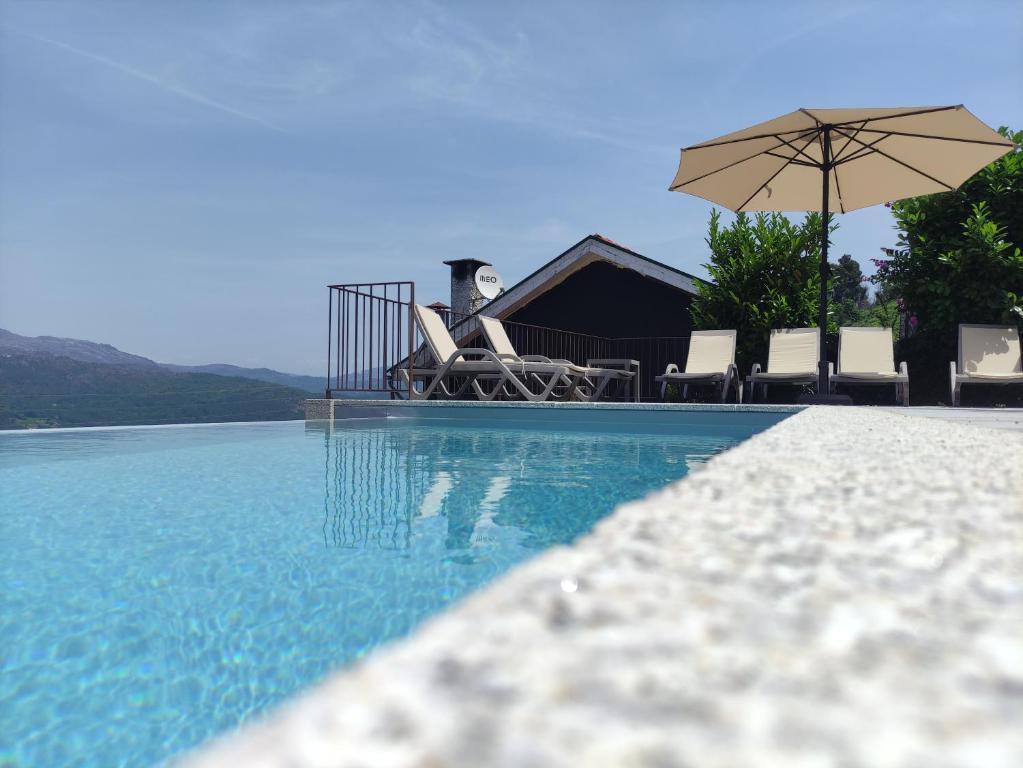 a swimming pool with chairs and an umbrella at Geres Andorinhas House in Vieira do Minho