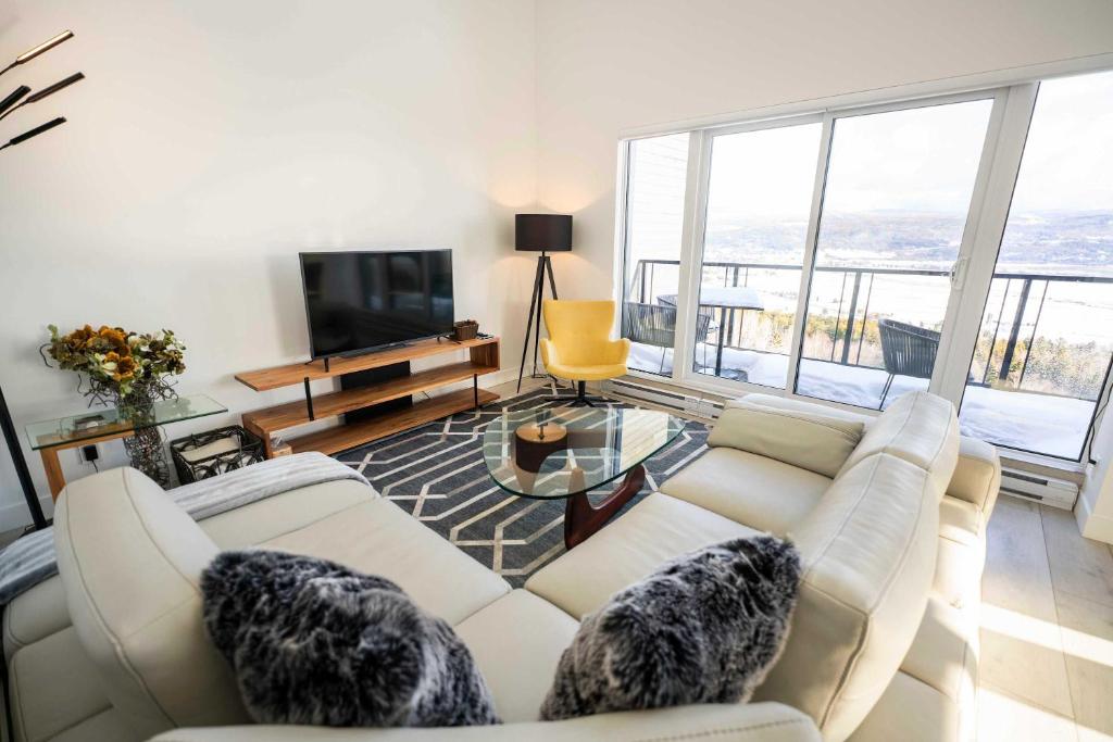 a living room with a white couch and a television at 401 - High-End Condo - Incredible View and Pool in Baie-Saint-Paul