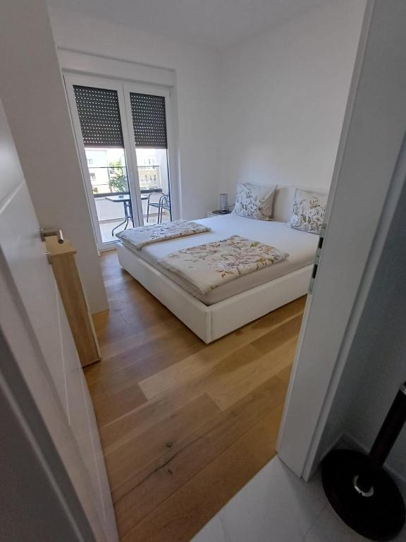 a white bedroom with a bed and a wooden floor at Apartman Sunce in Posušje