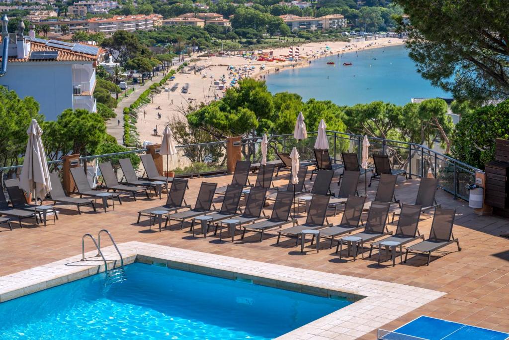 a swimming pool with chairs and a beach at GHT S'Agaró Mar Hotel in Sant Feliu de Guíxols