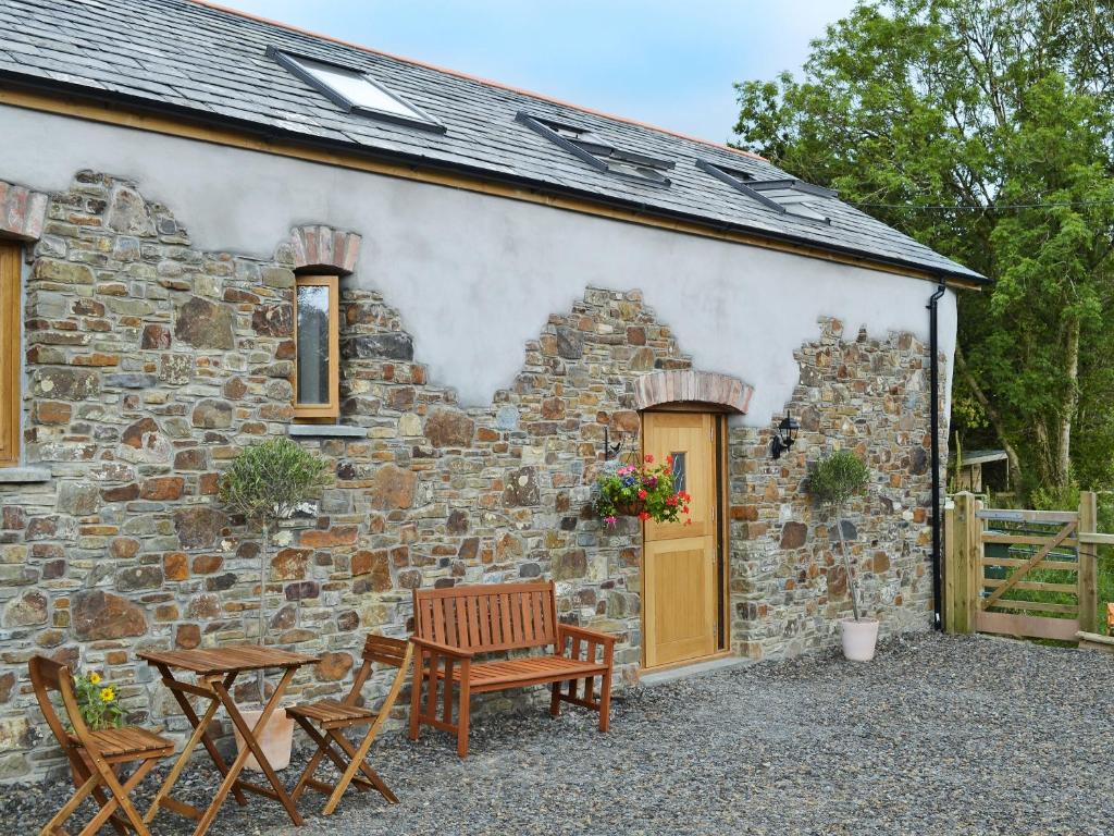 a stone building with two chairs and a table and a door at Stonechat Barn in Pancrasweek