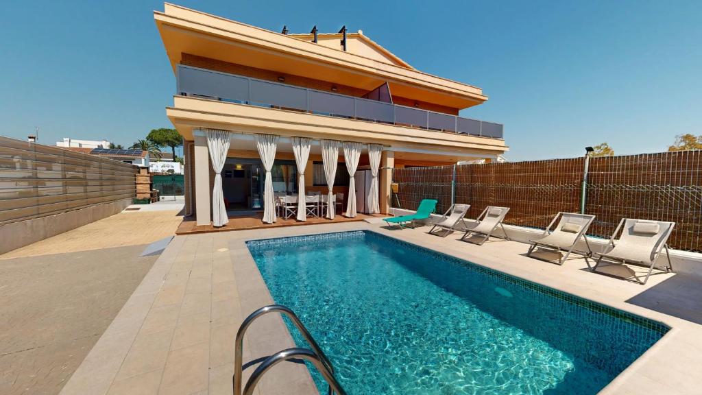 a swimming pool with chairs and a house at Villa Arenal in L'Ampolla