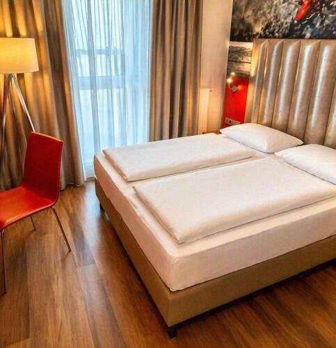 a bedroom with a bed and a red chair at DORMERO JeHo Graz Airport in Feldkirchen bei Graz