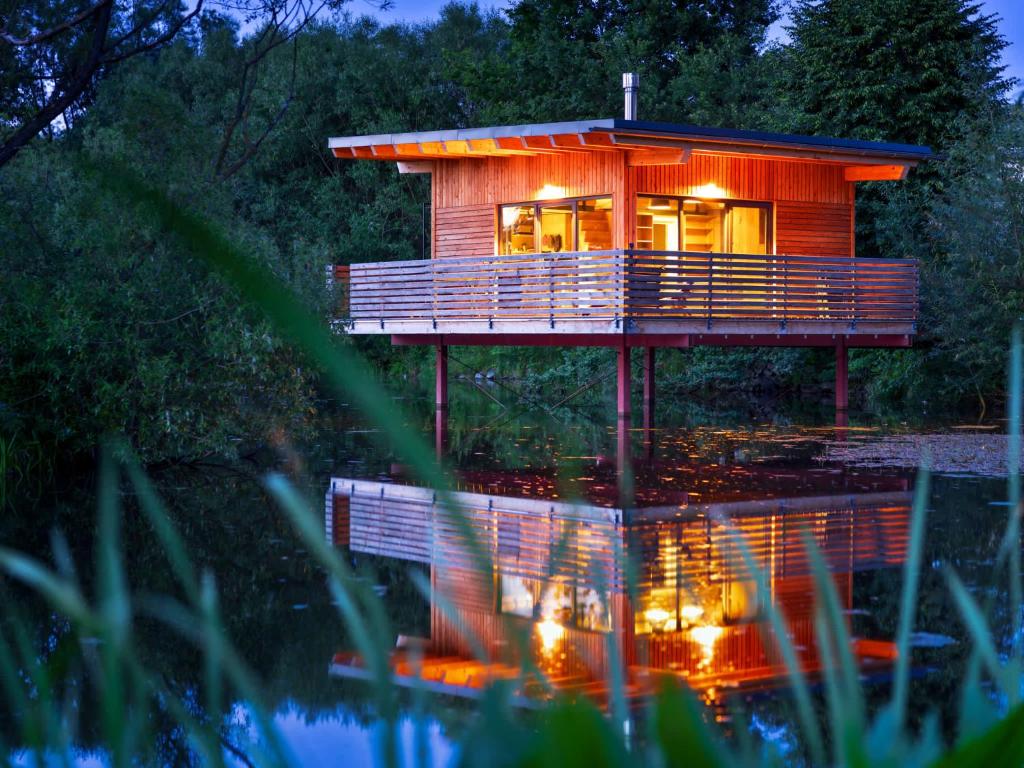 ein großes Holzhaus mit Lichtern am Wasser in der Unterkunft Spektakuläres Tiny House im Teich mit Terrasse und Kamin in Großharthau