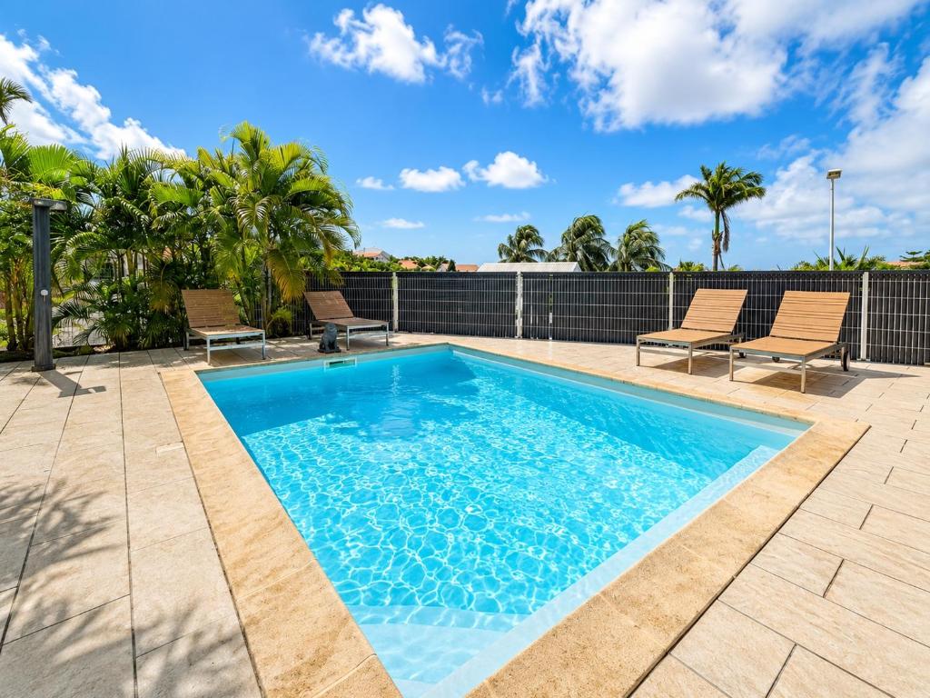 a swimming pool with two chairs next to a fence at VILLA CARAIBE in Sainte-Luce