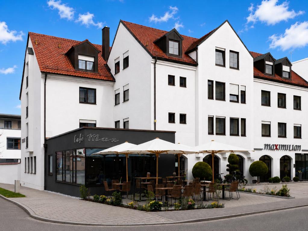 a large white building with tables and umbrellas at Hotel Garni Maximilian in Dingolfing