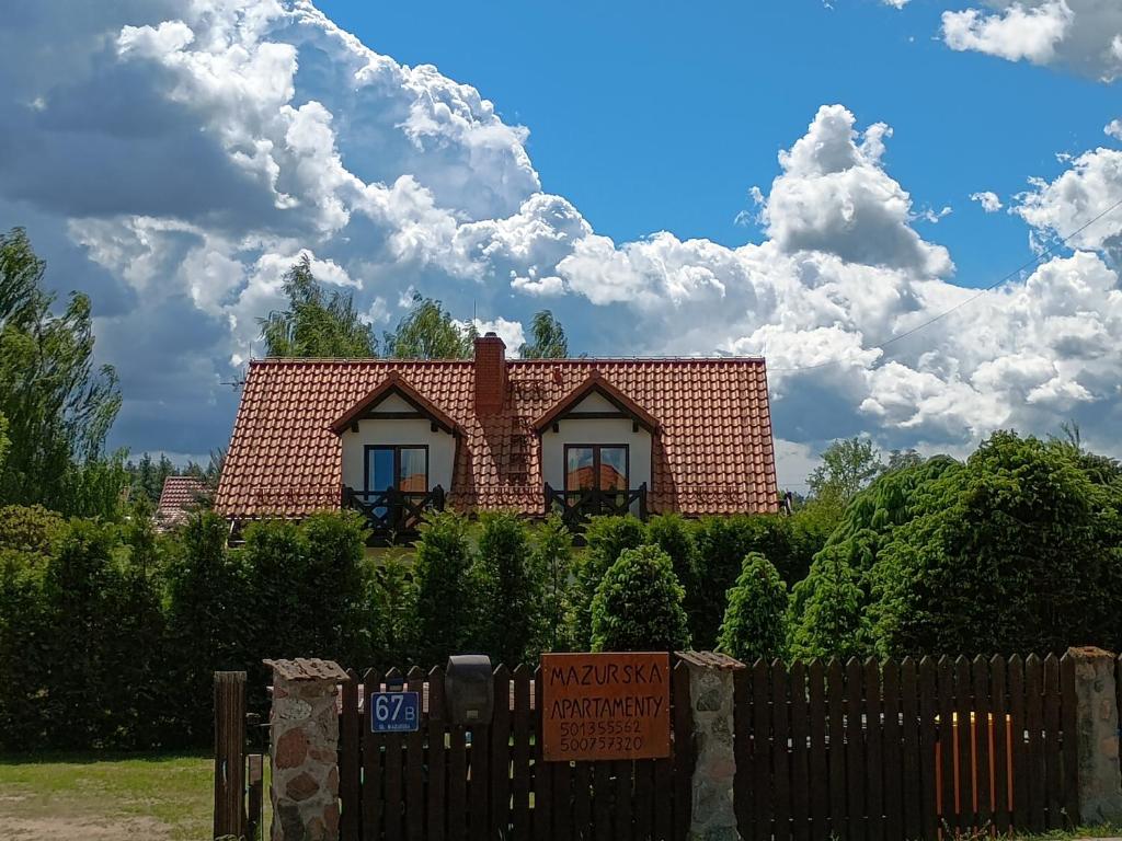a house with a sign in front of a fence at Mazurska Apartamenty in Rydzewo