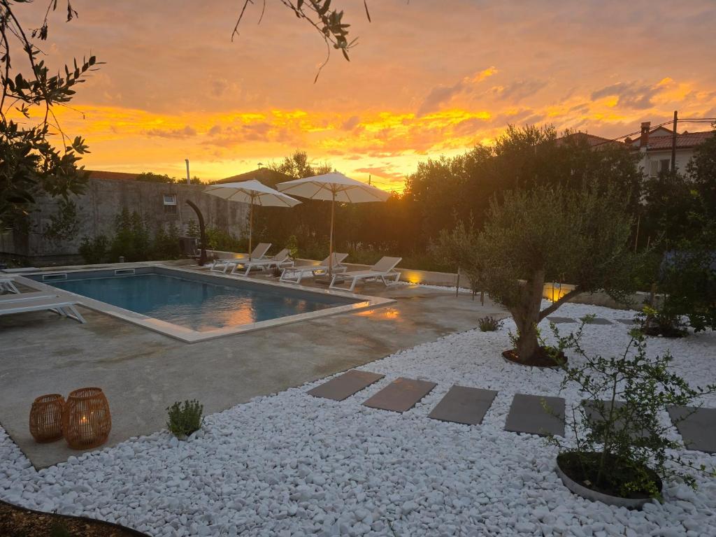 a pool with chairs and a sunset in the background at Villa Castelana in Barbat na Rabu