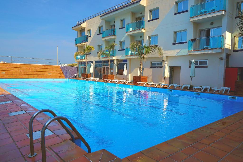 a large blue swimming pool next to a building at Hotel Port Sitges in Sitges
