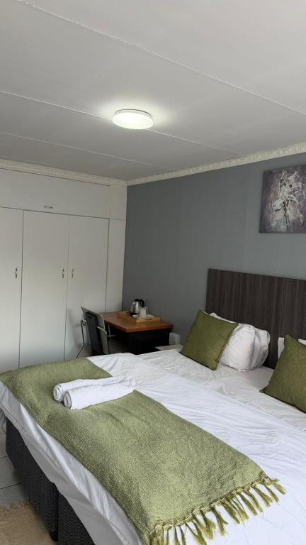a large white bed with a green blanket on it at Host Hub Guest House in Kempton Park
