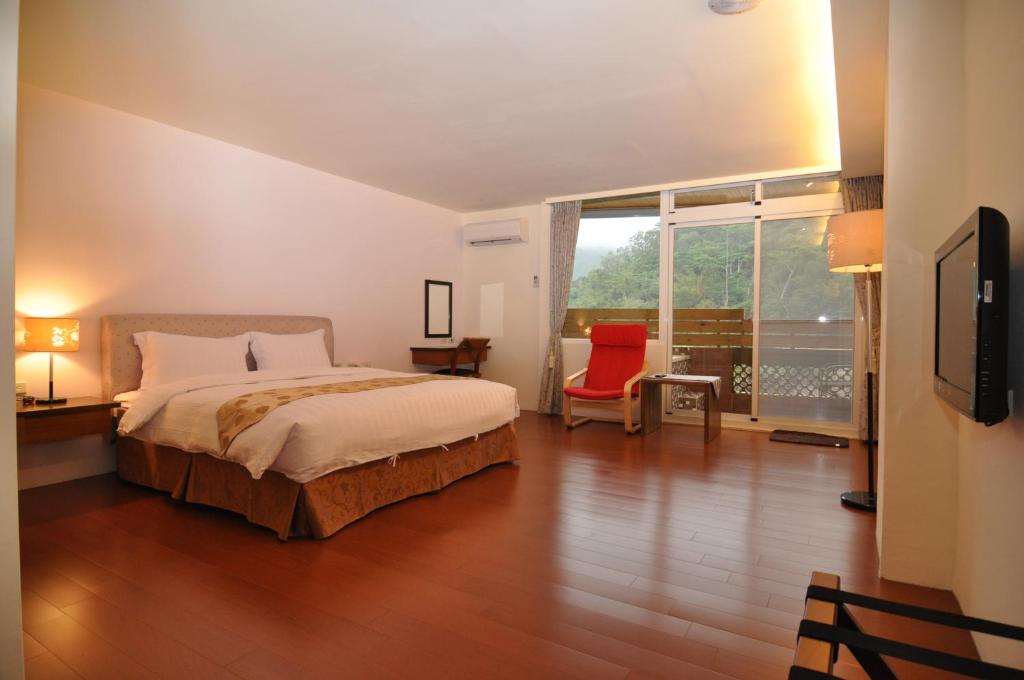een slaapkamer met een groot bed en een rode stoel bij Cheng-Ping Hot Spring Inn in Wenquan