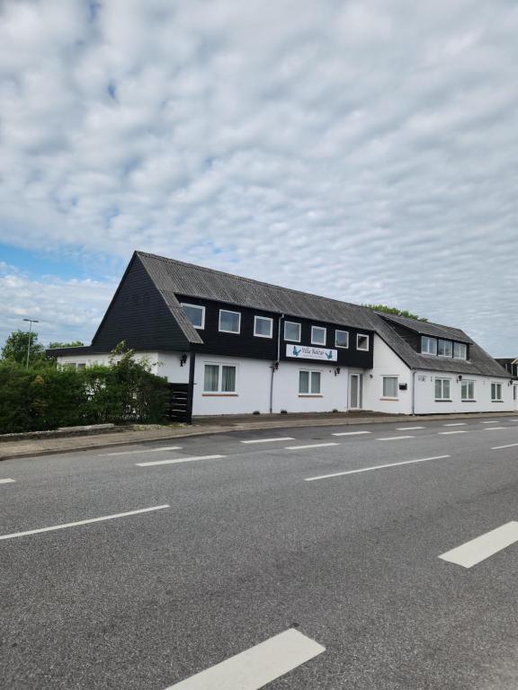 a white building with a black roof on the side of a road at Ferielejlighed ved Vilsted Sø in Løgstør
