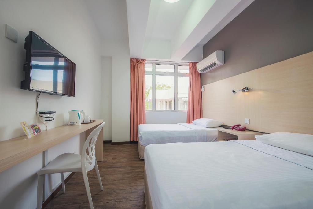 a hotel room with two beds and a desk and a television at YMCA Penang in George Town