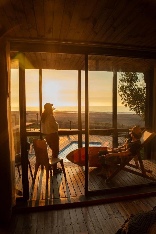 a couple of people standing on a screened in porch with the sunset at Hotel Punta Sirena in Curanipe