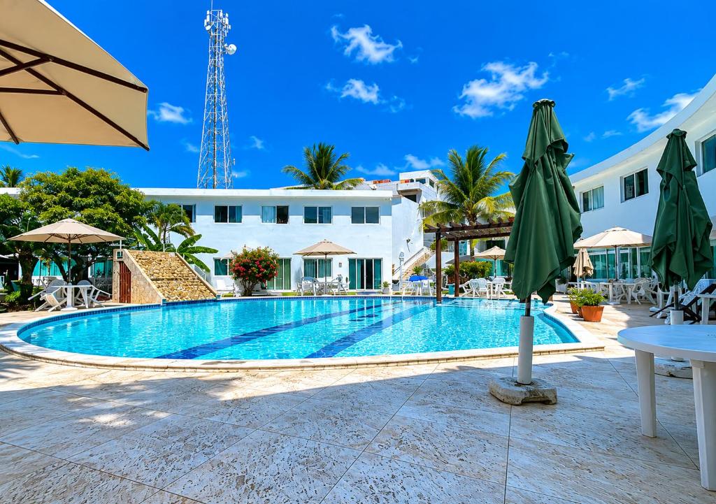 a swimming pool with a table and umbrellas and a building at Mandakaru Residence Flat da Isa 01 in Porto De Galinhas