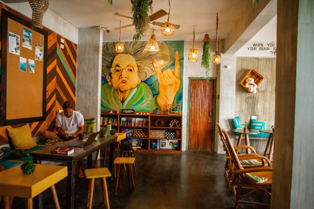 a man sitting in a room with a large painting on the wall at Happiness Hostel El Nido in El Nido