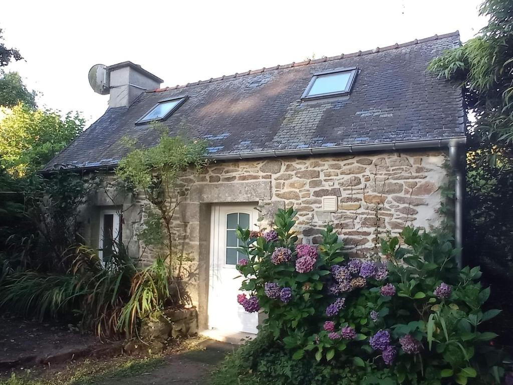 a stone cottage with a white door and purple flowers at Nice cottage in Brittany in Plouigneau
