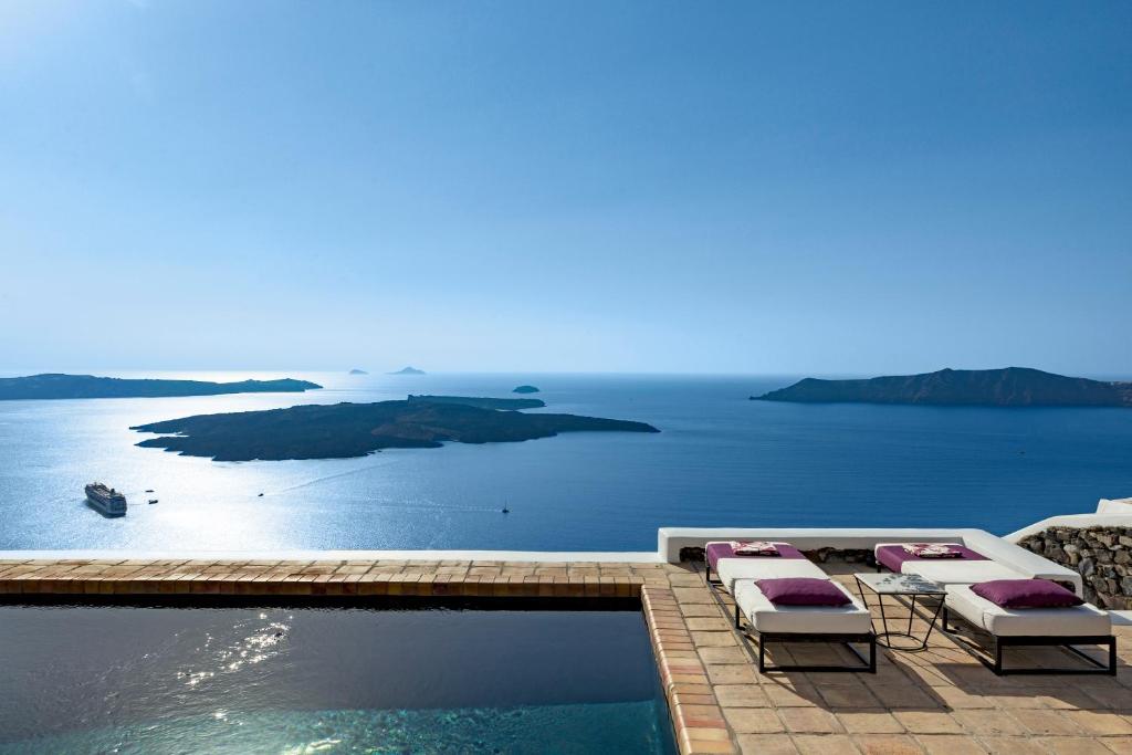 a pool with lounge chairs and a view of the ocean at The Vasilicos in Imerovigli