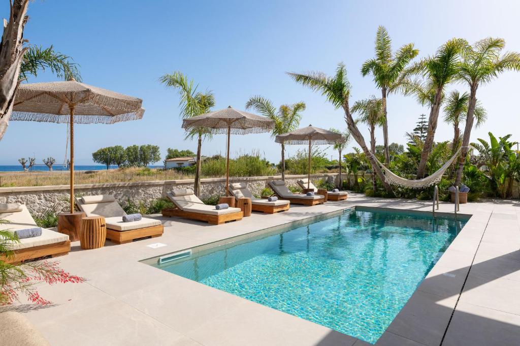 an infinity pool with lounge chairs and umbrellas at Palmeral Luxury Villas in Kremasti