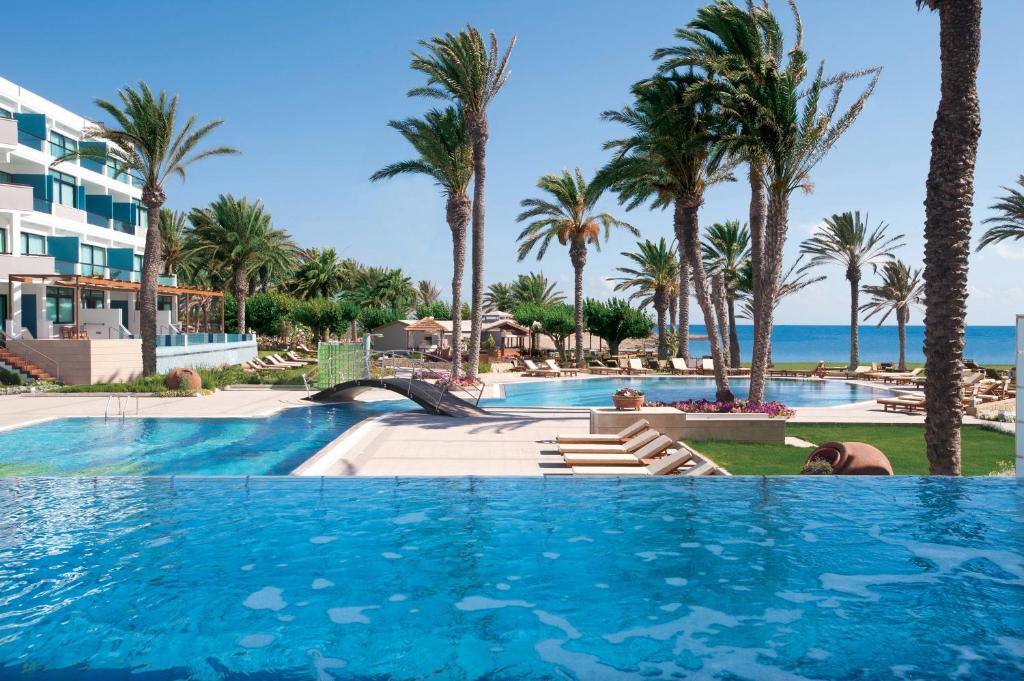 uma piscina num resort com palmeiras e o oceano em Constantinou Bros Asimina Suites Hotel em Pafos