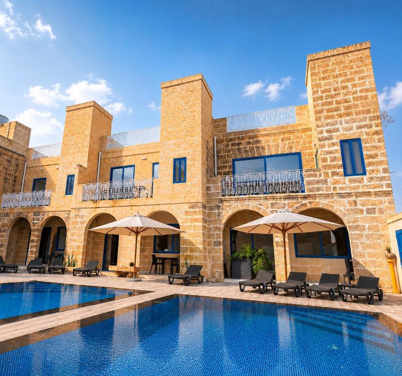a pool in front of a brick building with umbrellas at Fiftyfour West Boutique Living in Għarb