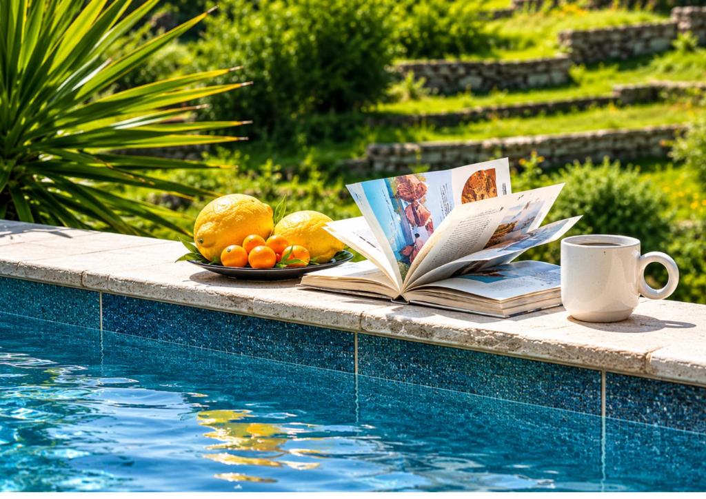 a plate of fruit and a book next to a swimming pool at Garden Residence Andros with Sea View & Pool in Gavrio