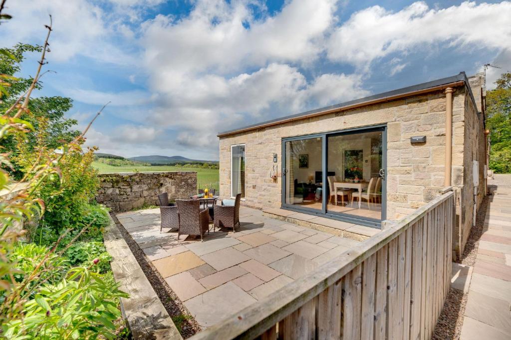 a stone cottage with a patio and a dining area at Gardener's Cottage in Alnwick