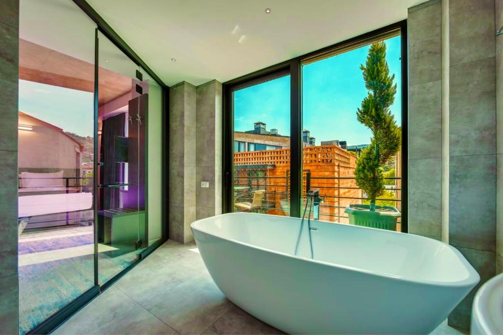 a bath tub in a bathroom with large windows at Mit Hotel Tbilisi in Tbilisi City