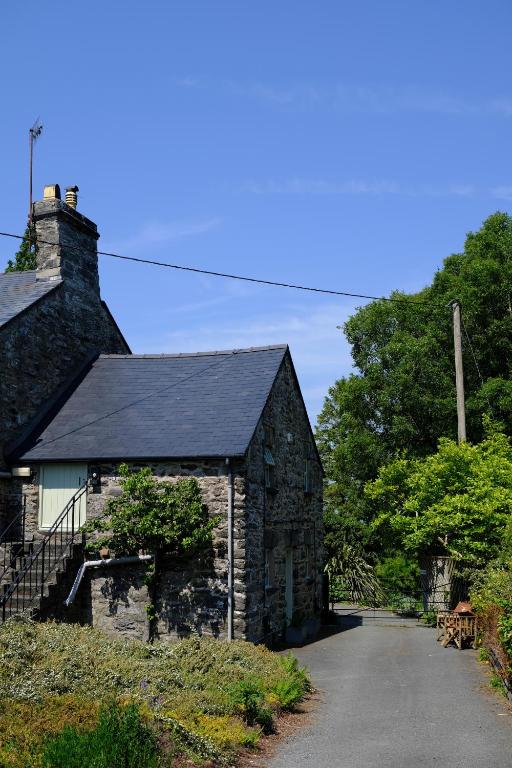 an old stone building with a black roof on a road at Eryri Golden Stays in Capel Garmon