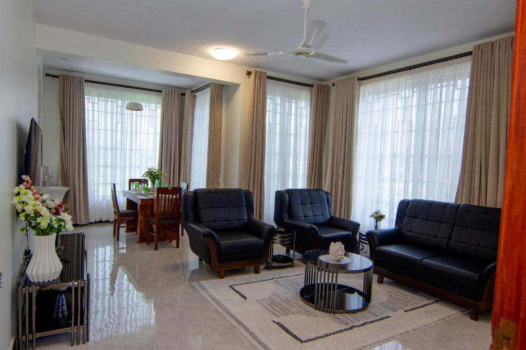 a living room with chairs and a table and windows at JJC BNB Mbweni in Bunju