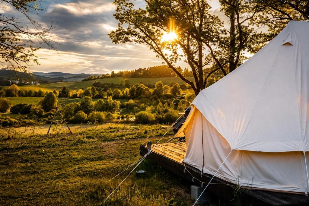 a white tent in a field with the sun setting at Glamping Hive in Čmeliny
