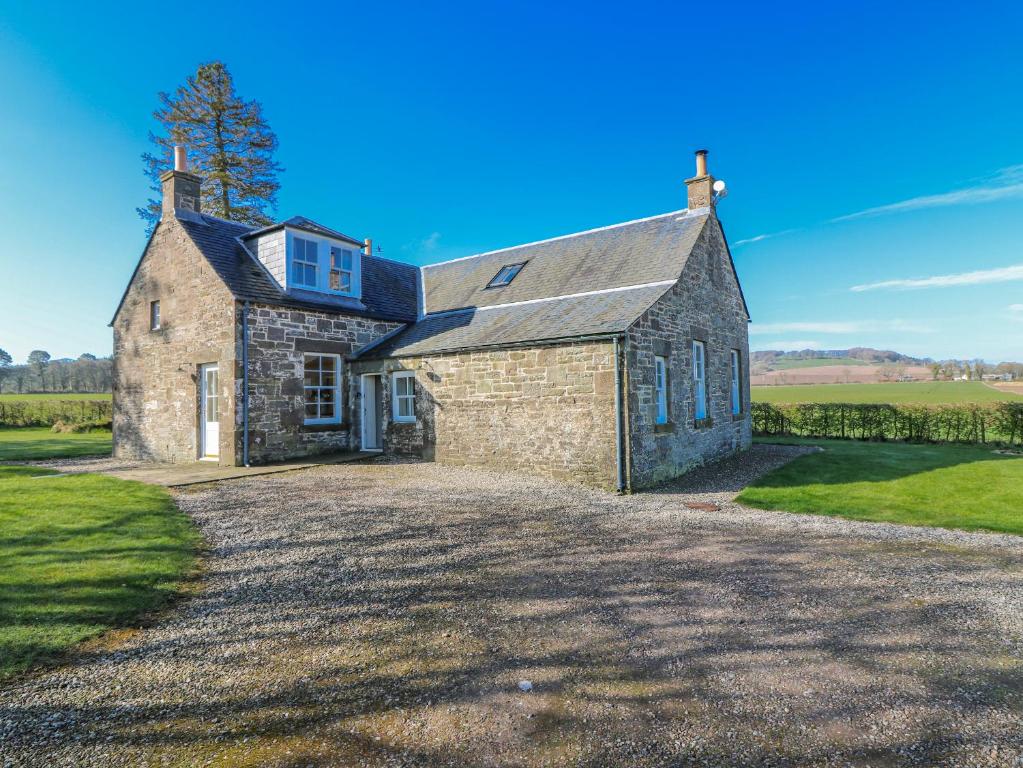 an old stone house with a gravel driveway at Meadowgreen Farmhouse in Forfar
