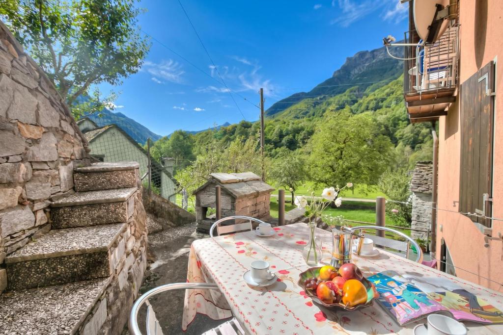a table with a bowl of fruit on a balcony with mountains at Ca Contina in Val Verzasca - Happy Rentals in Frasco