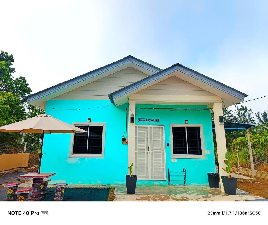a blue house with a table and an umbrella at BABA Homestay in Kuala Kerai