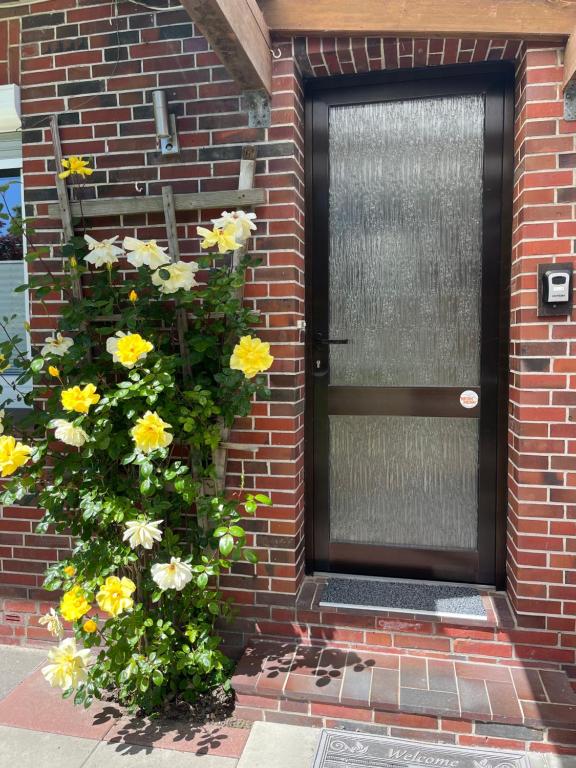 a front door of a brick house with yellow flowers at Wohnung 1 mit überdachte Terrasse zum Garten Nähe Strand und Hafen Bensersiel in Bensersiel
