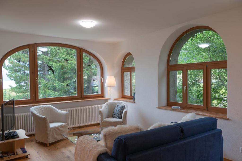 a living room with three arched windows and a blue couch at Chesa Clos in Sils Baselgia