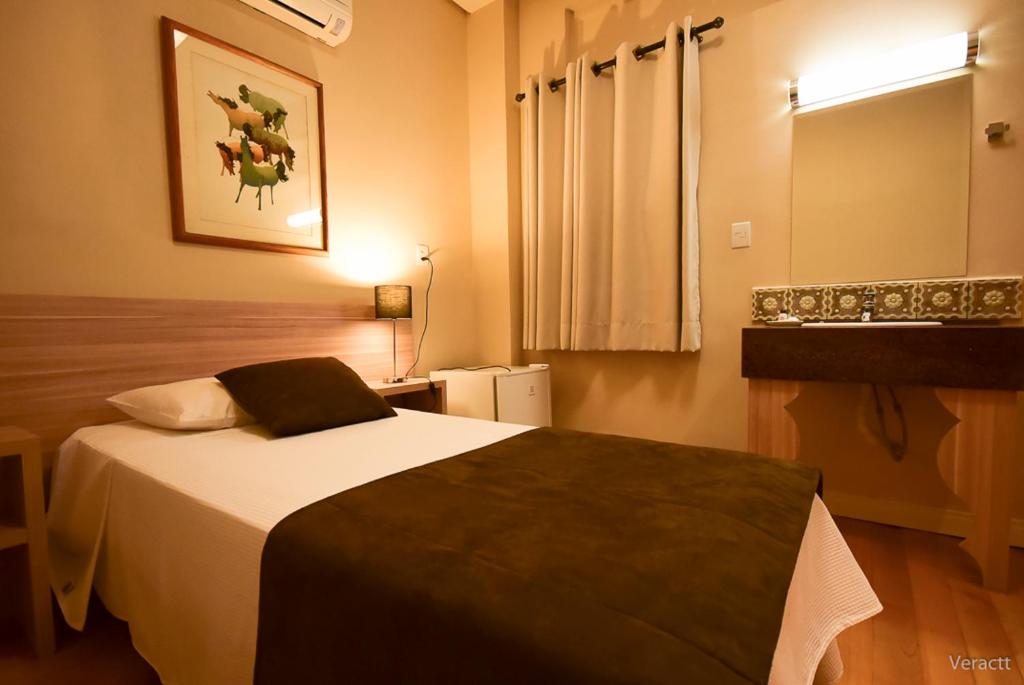 a bedroom with a bed in a room with a window at Hotel Praça da Matriz in Porto Alegre