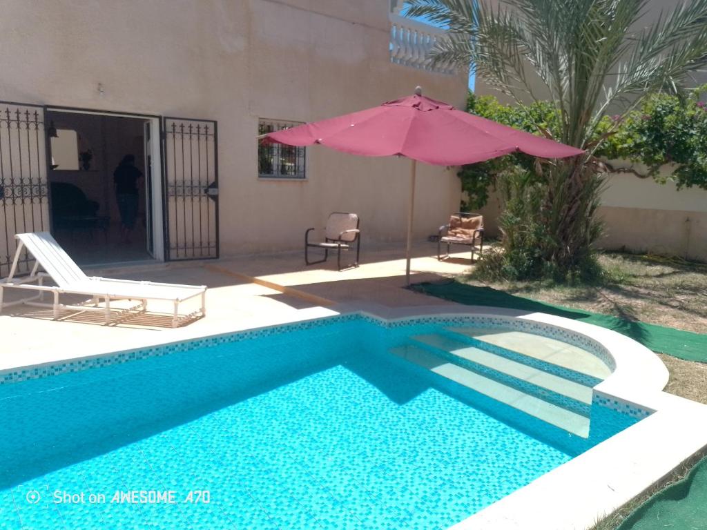 a swimming pool with an umbrella and a house at villa Flori Midoun in Djerba