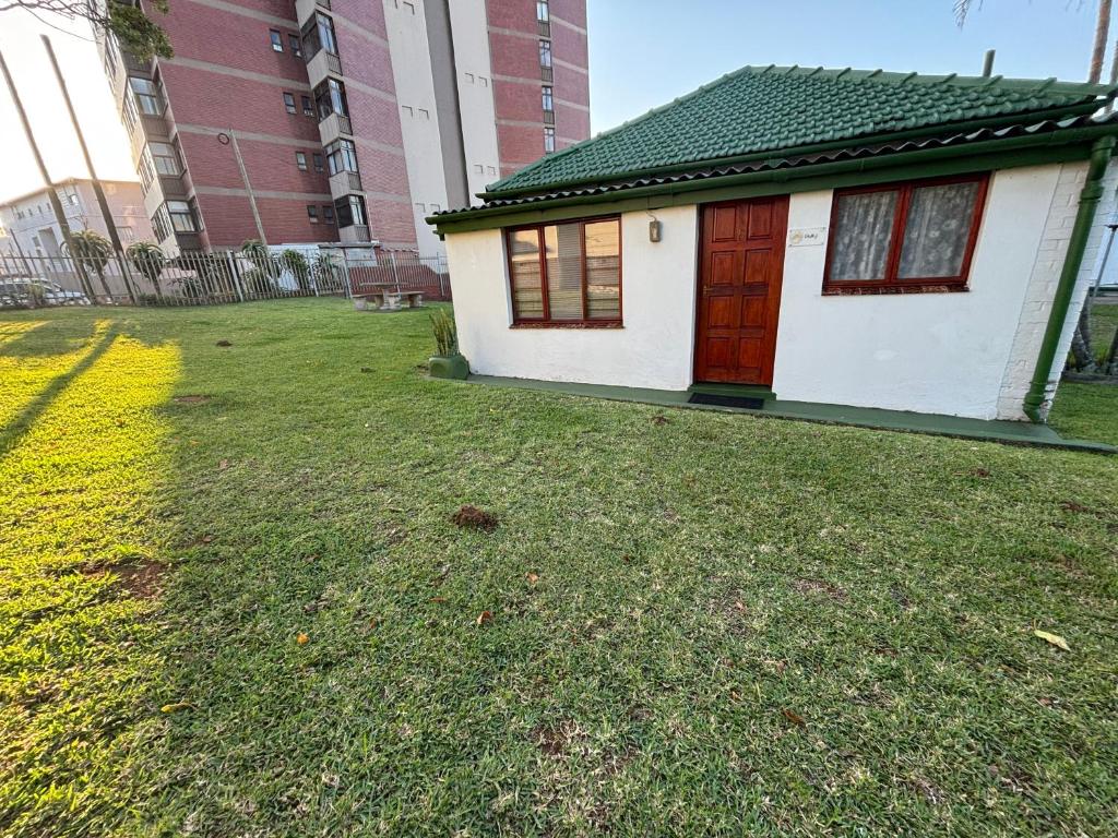 a small white house with a red door in a yard at Siesta Island #5 in Amanzimtoti
