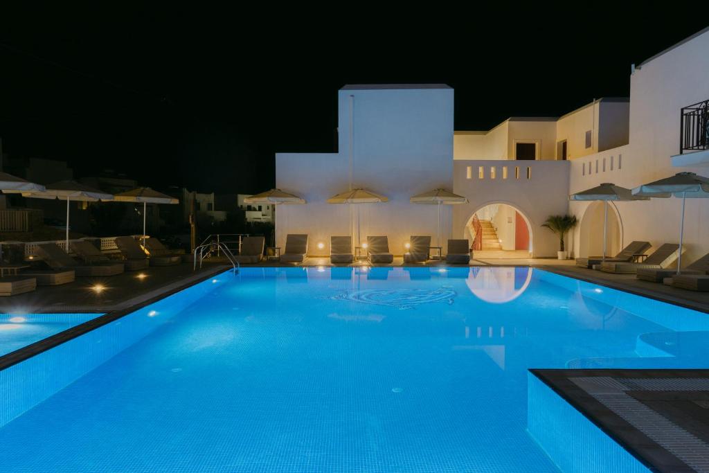 una piscina de noche con sillas y sombrillas en Perla Hotel, en Agios Prokopios