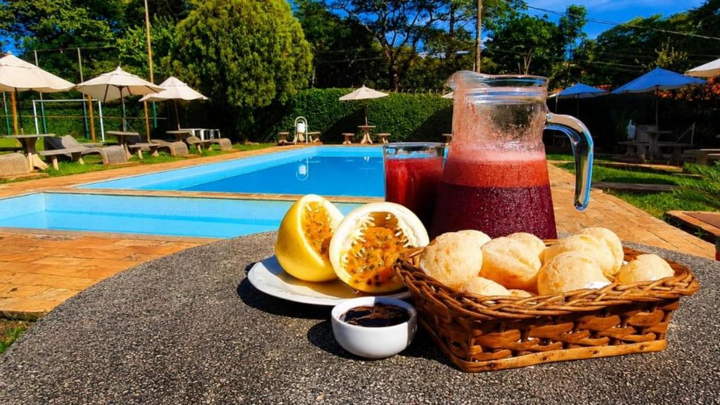 a basket of bread and a drink on a table near a pool at Pousada Sant`Ana in Sabará