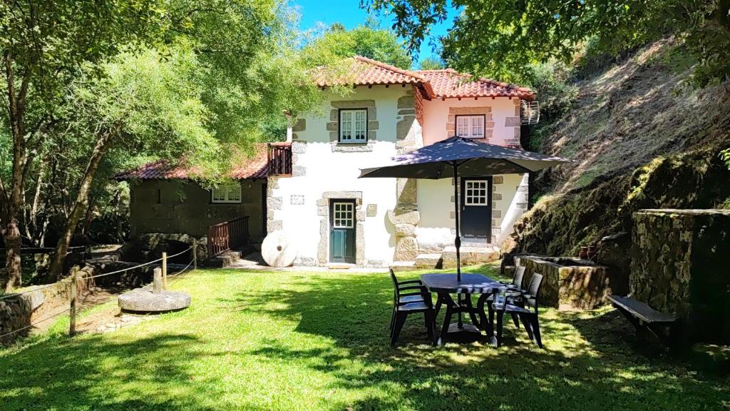 a house with a table and chairs and an umbrella at Moinho da Cruz in Ponte de Lima